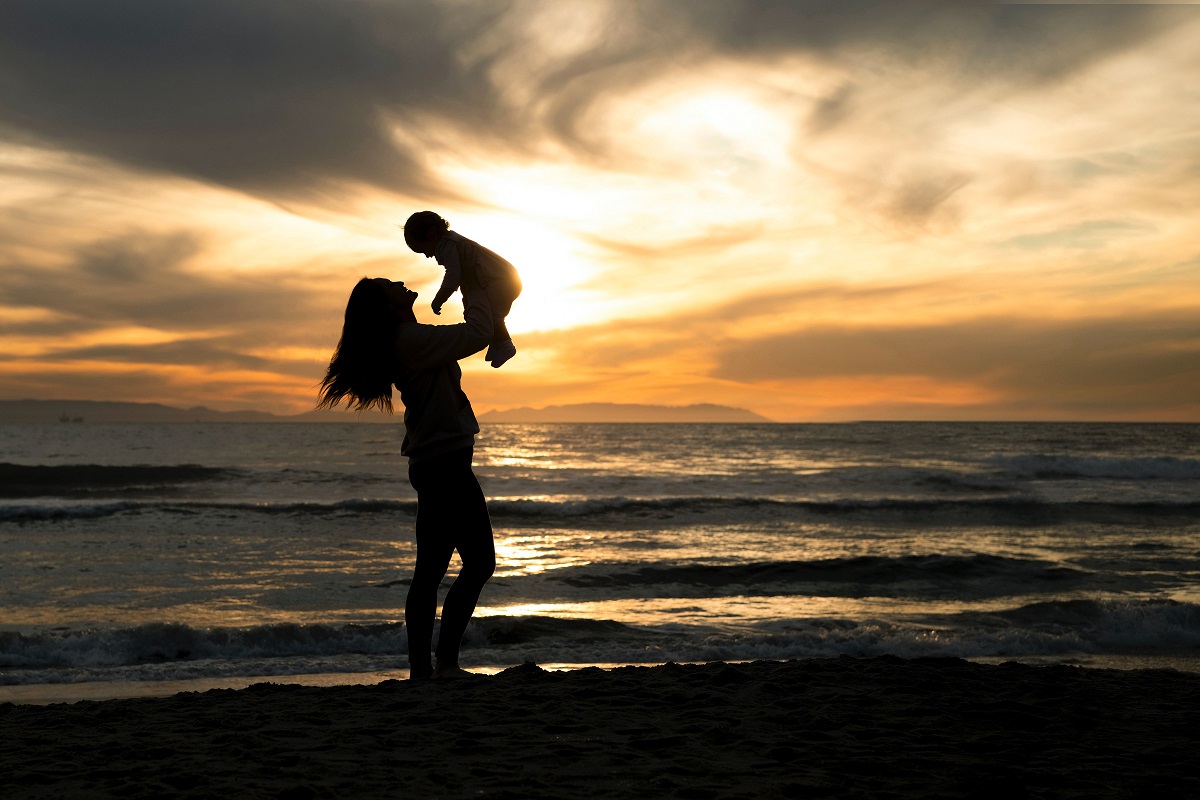 mamma con bambino in braccio al mare, sullo sfondo sole e nuvole scure